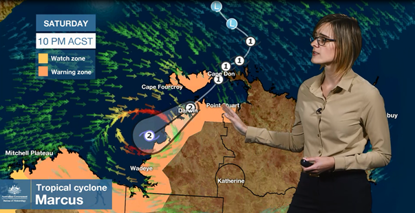 Woman points at a weather map showing the track of a cyclone and areas of the Northern Territory that are watch and warning zones.